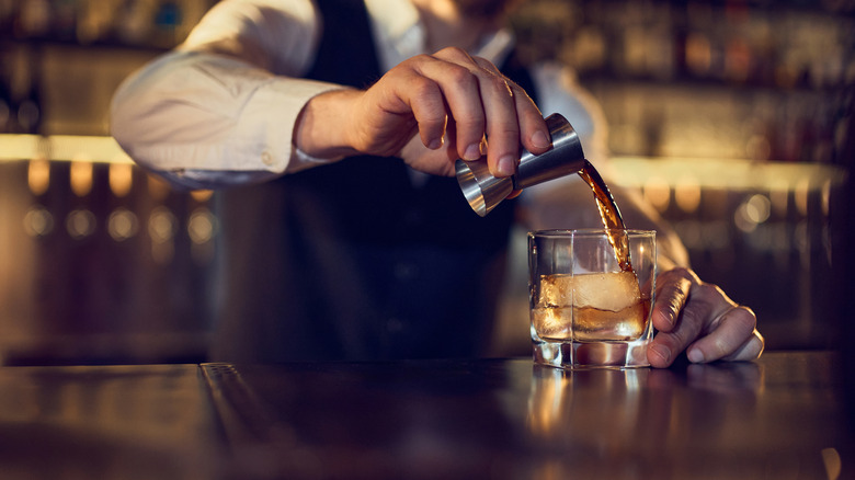 A bartender pouring a drink using a jigger