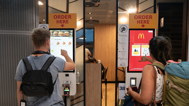 People ordering food from a digital kiosk inside McDonald's.