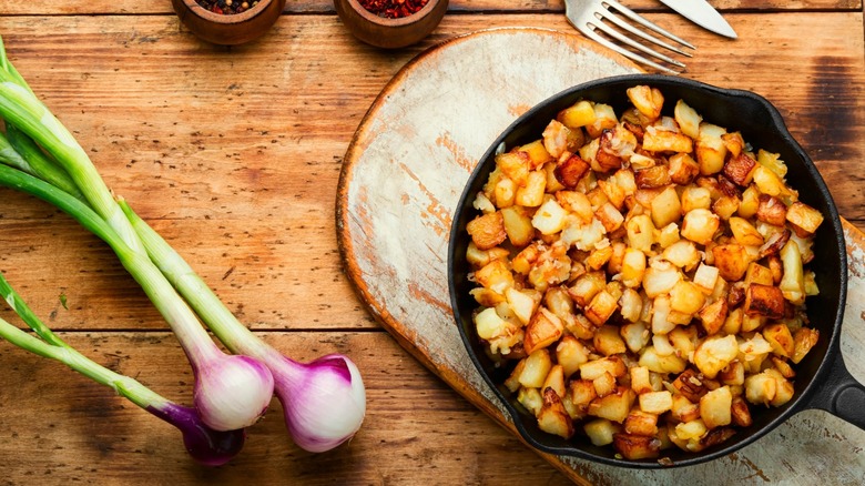 Skillet potatoes next to onion bulbs