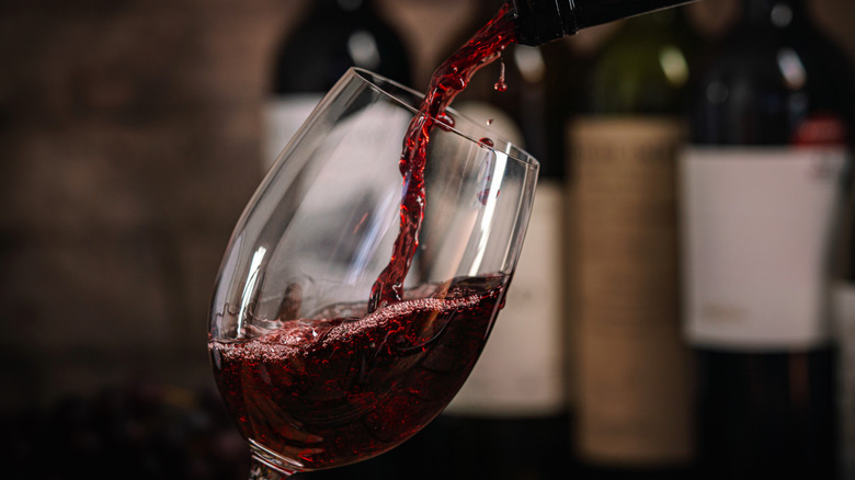 Red wine being poured into a glass against the backdrop of other bottles of wine.