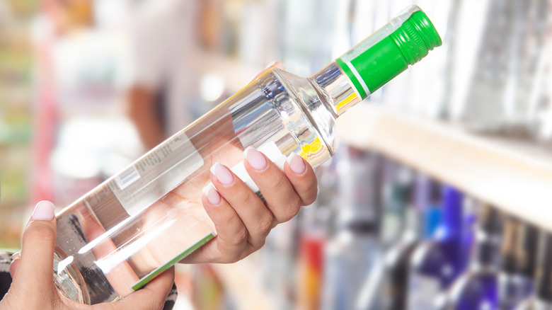 Person inside liquor store reading the label on a bottle of vodka.