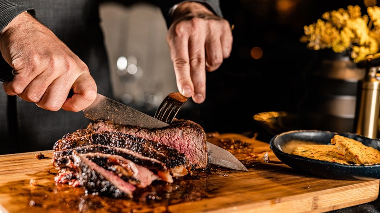 A chef slices a grilled steak on a wooden cutting board in a steakhouse