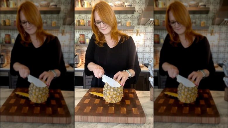 Ree Drummond slicing the skin off a pineapple.