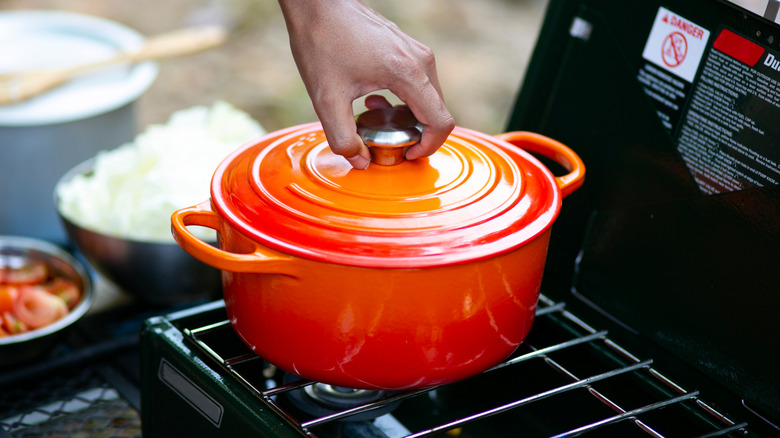 Person touching the lid of an enameled cast iron pot sitting on outdoor grill