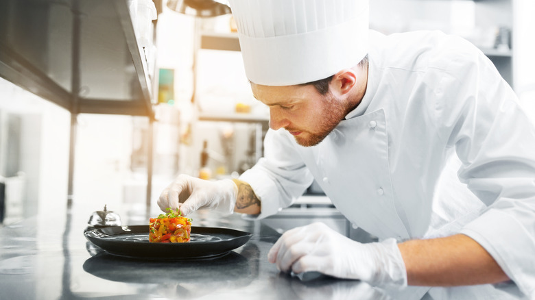 Chef in chef's hat garnishing dish