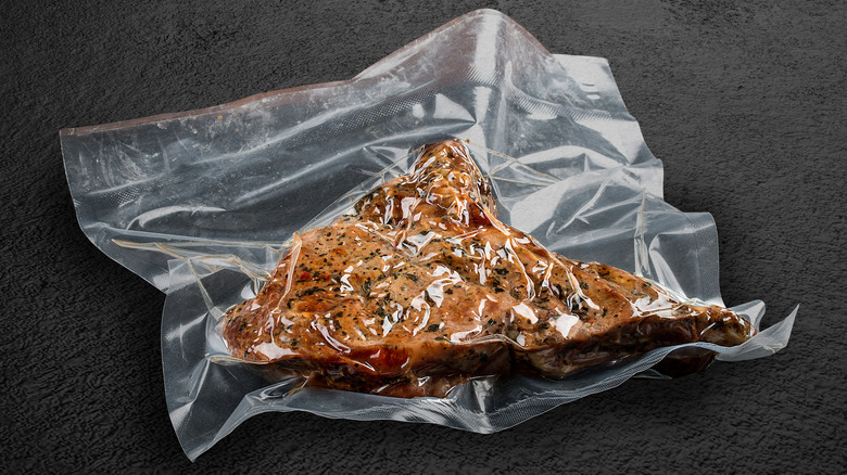 A cooked steak vacuum-sealed in plastic on a black countertop.