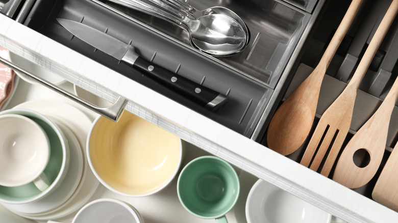 Stacked kitchen drawers with utensils, plates, and mugs
