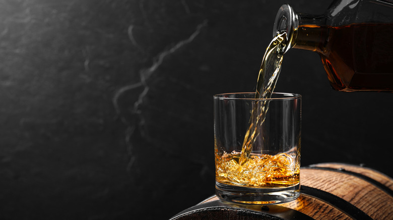 Pouring bourbon into glass tumbler on top of a barrel