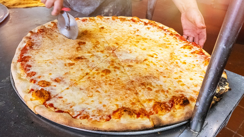 person cutting large new York style pizza
