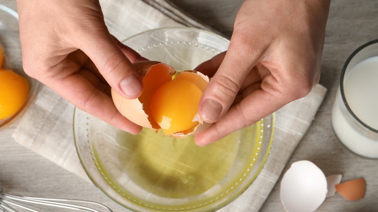 Hands separating an egg yolk with the shell over a glass bowl