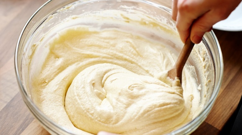 Hand stirring cake batter in a glass bowl with a wooden spoon