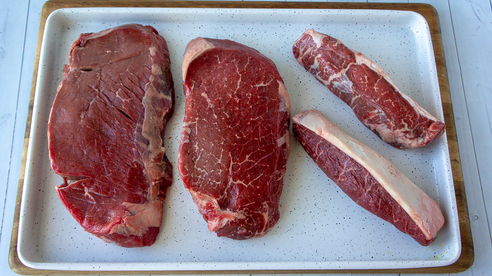 a white sheet pan with 4 steaks on it