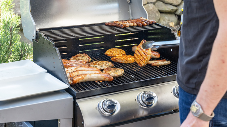 Person cooking meat on a propane grill and lifting a patty with tongs