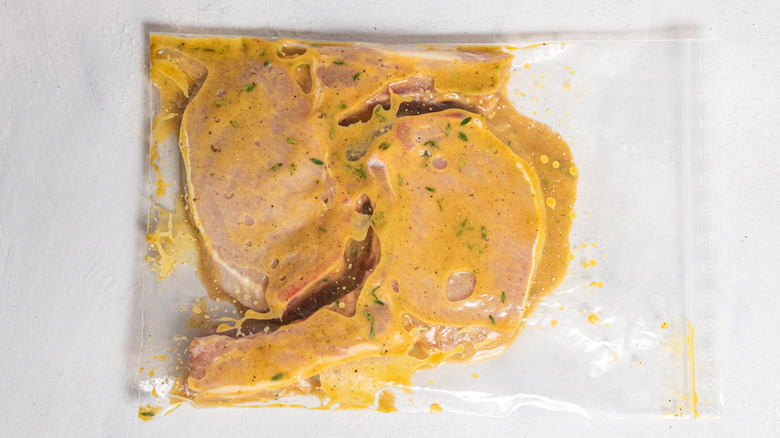 Two pork chops marinating in a plastic bag with a honey mustard marinade