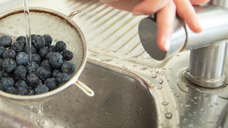 Person washing blueberries in a sieve under water