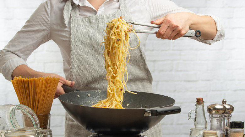 Woman lifting pasta from a pan with tongs
