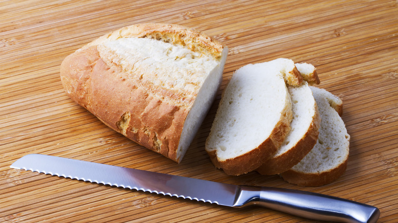 A serrated knife and a loaf of bread on a wooden background