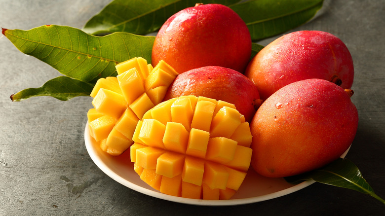 Sliced and whole mangos in bowl next to mango leaves