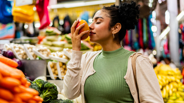 Customer smelling mango in produce section of supermarket