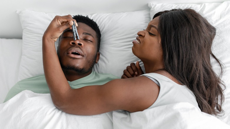   Mand snorker og kvinde sætter tøjklemme på hans næse
