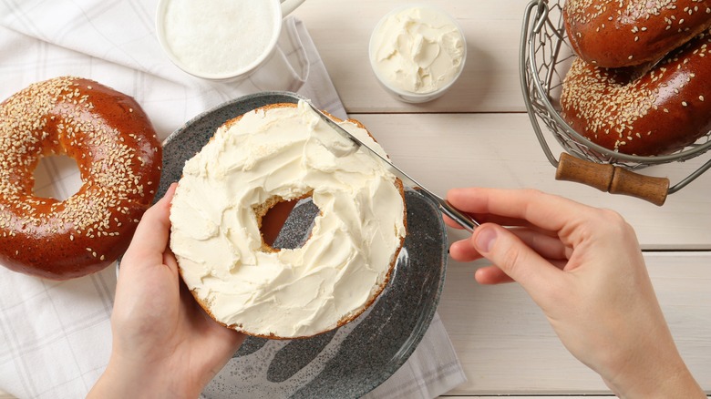 Hands putting cream cheese on a bagel