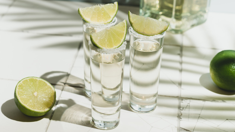 3 tequila shots topped with lime and more limes in the background