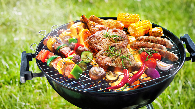 Meat and veggies on outdoor grill with grass in background