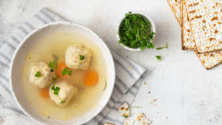 Bowl of matzo ball soup nest to parsley and matzo boards