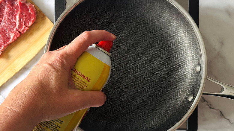 hand spraying a frying pan with oil