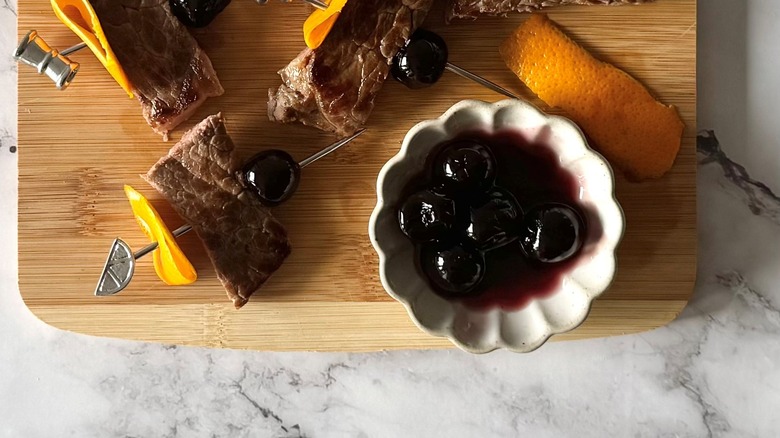 steak, orange slices, and cherries on metal skewers