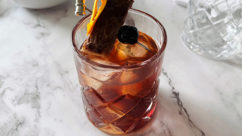 brown cocktail garnished with steak and orange