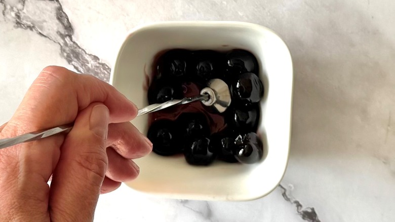 hand holding a muddler in a cup of cherries
