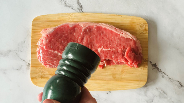 hand holding a salt grinder over a steak