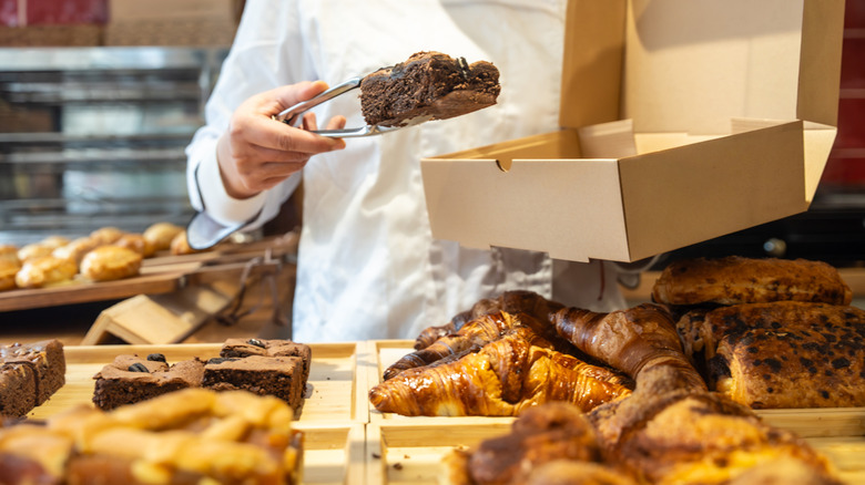 Baker boxing up one of many baked goods at counter