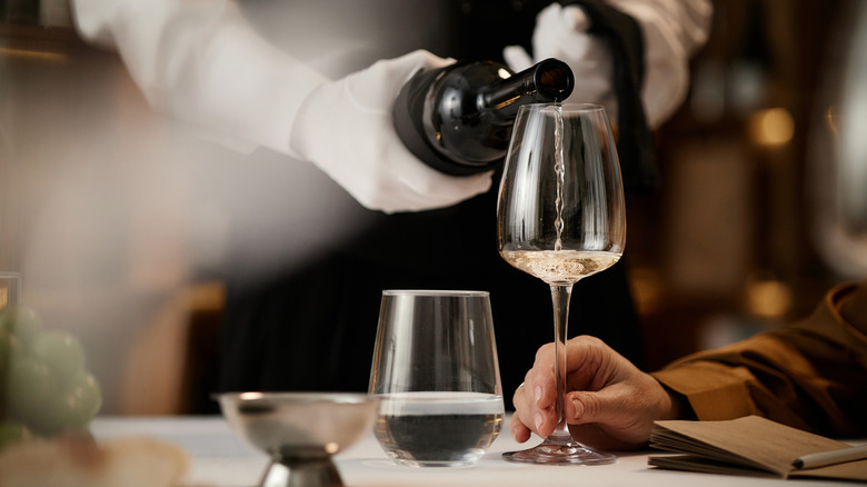 White gloved waiter pours white wine into glass for tasting