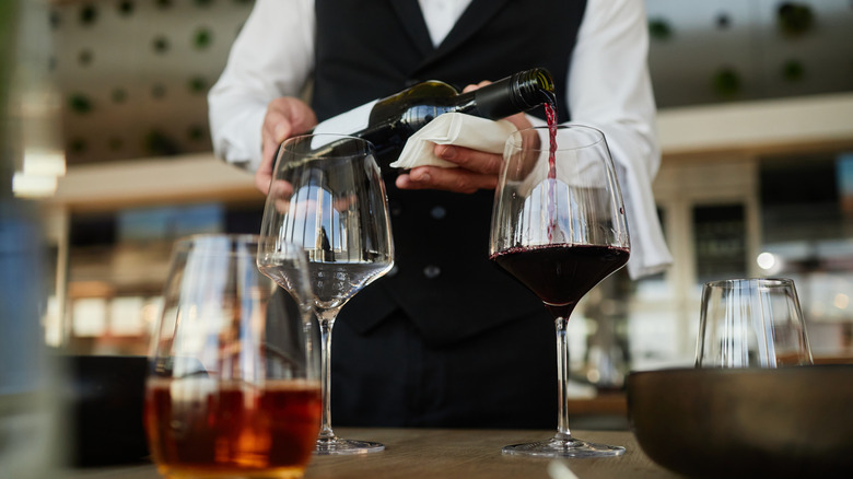 Waiter pouring bottle of red wine into glass at restaurant table