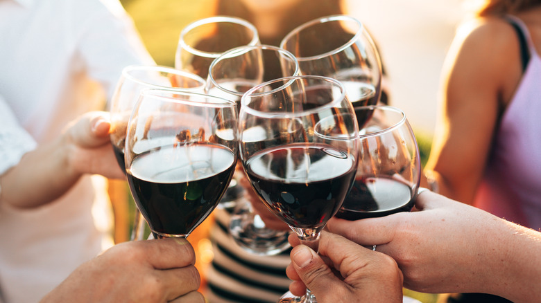 Group of people toasting wine glasses with red wine.