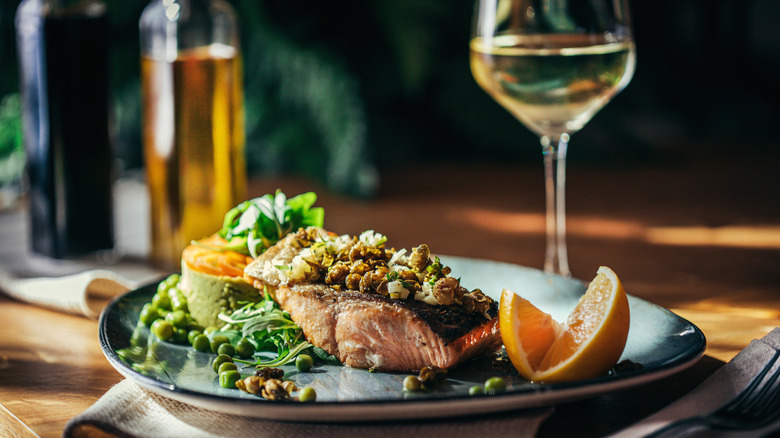 An elaborate salmon dish and glass of white wine on table