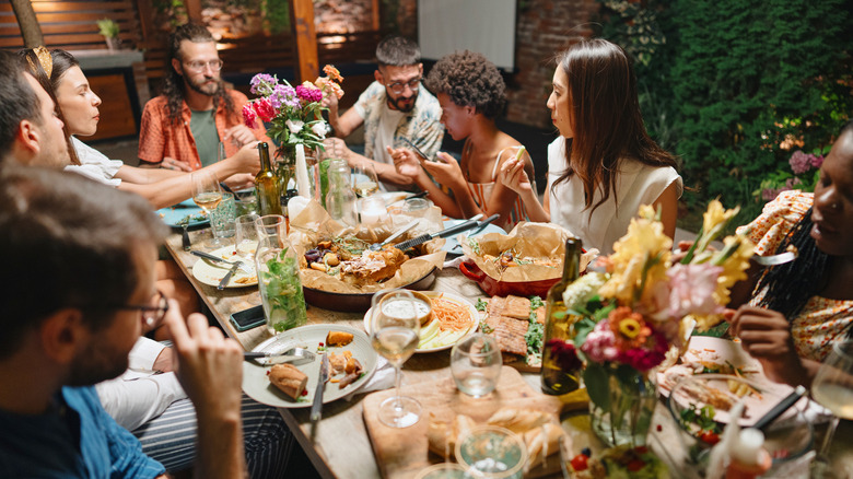 Friends at a dinner party with wine and several plates of food on crowded table