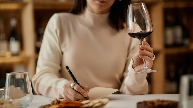 Woman holding a glass of red wine and taking notes
