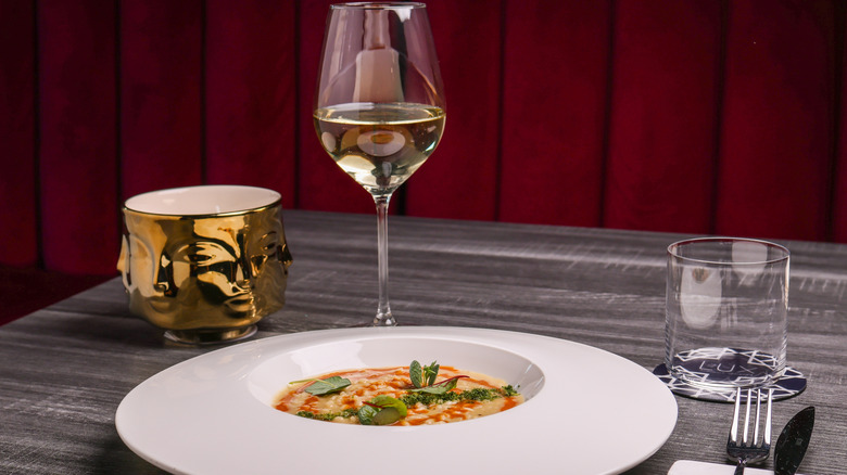 Risotto in white plate and a glass of white wine on table