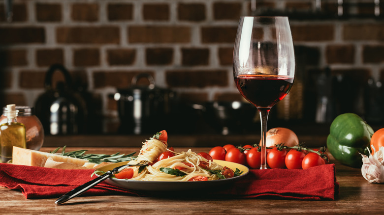 Plate of spaghetti and glass of red wine on wooden table with whole veggies and block of aged cheese
