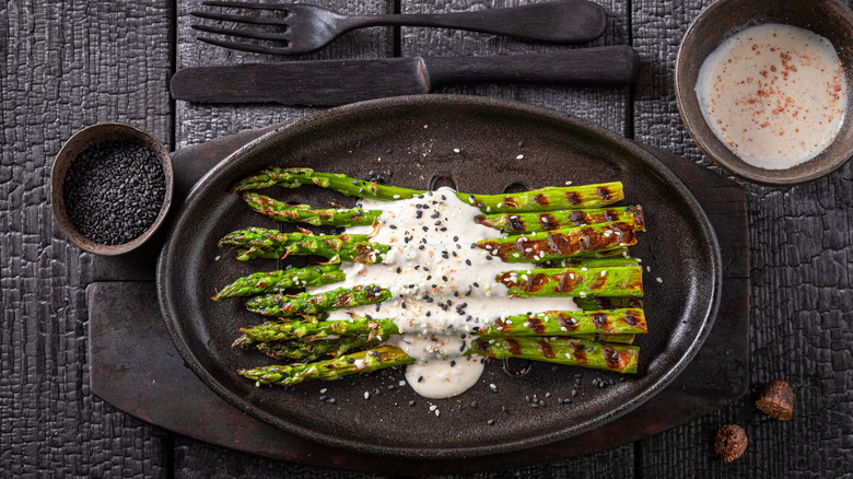 Plate of grilled asparagus with elaborate presentation topped with white sauce and sesame seed garnish