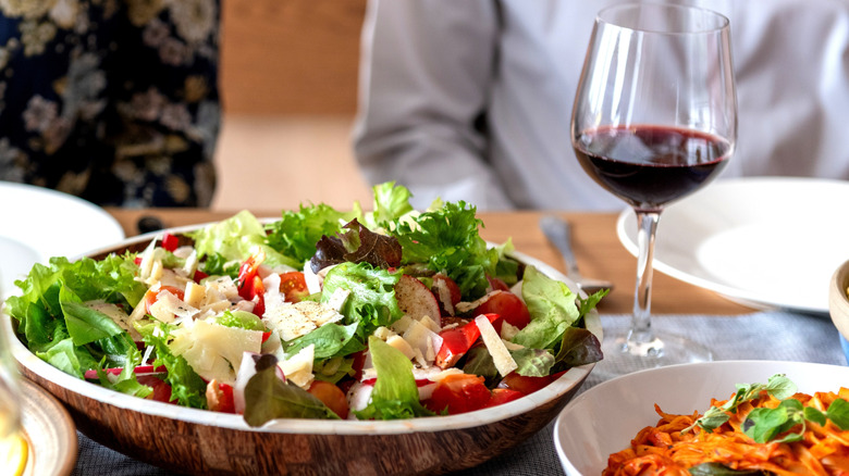 Close up of a salad with freshly grated parmesan and a glass of red wine on table