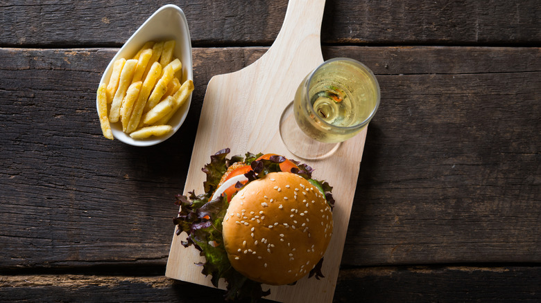 Aerial view of cutting board with glass of sparkling wine and a burger next to side of fries