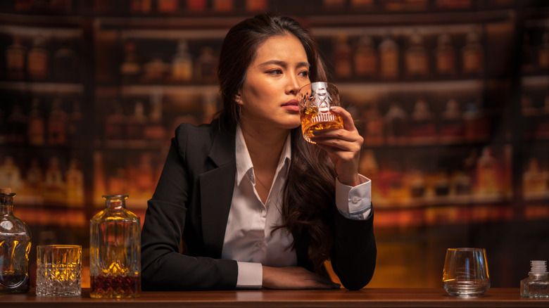 Woman in suit sipping bourbon in a bar