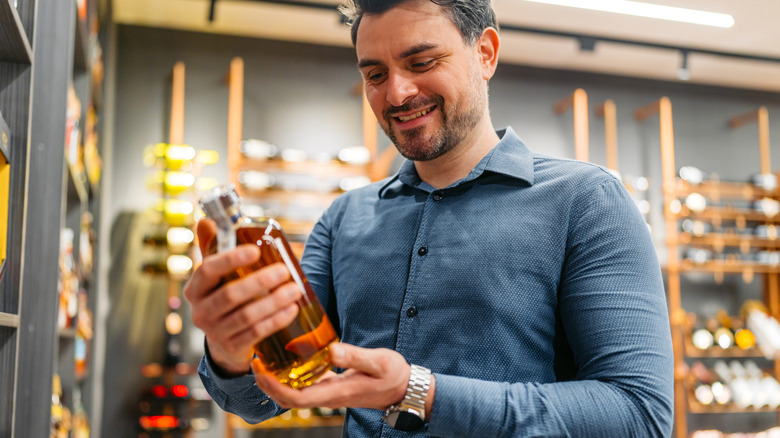 Man reading label on bourbon bottle in liquor store