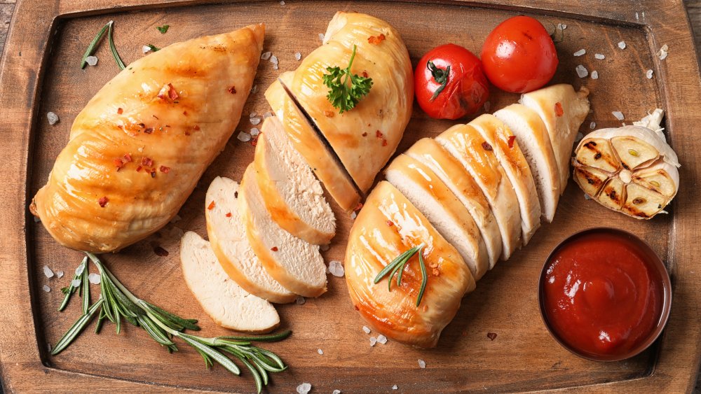 Cooked chicken breast with rosemary and tomato on cutting board