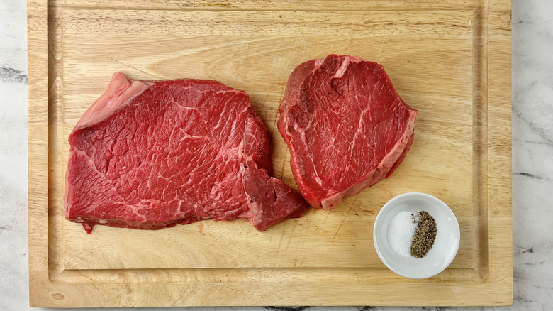 Steaks and bowl of salt and pepper on wooden board