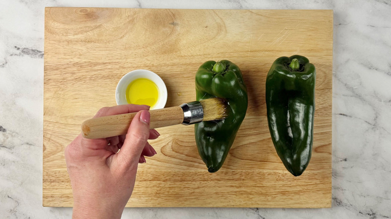 Hand brushing poblano peppers with oil